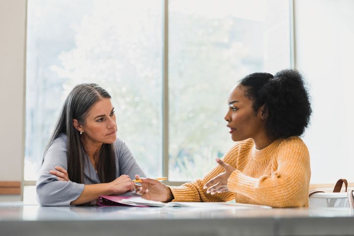 A female teacher or counsellor is talking to a female student who is wearing a yellow sweater.